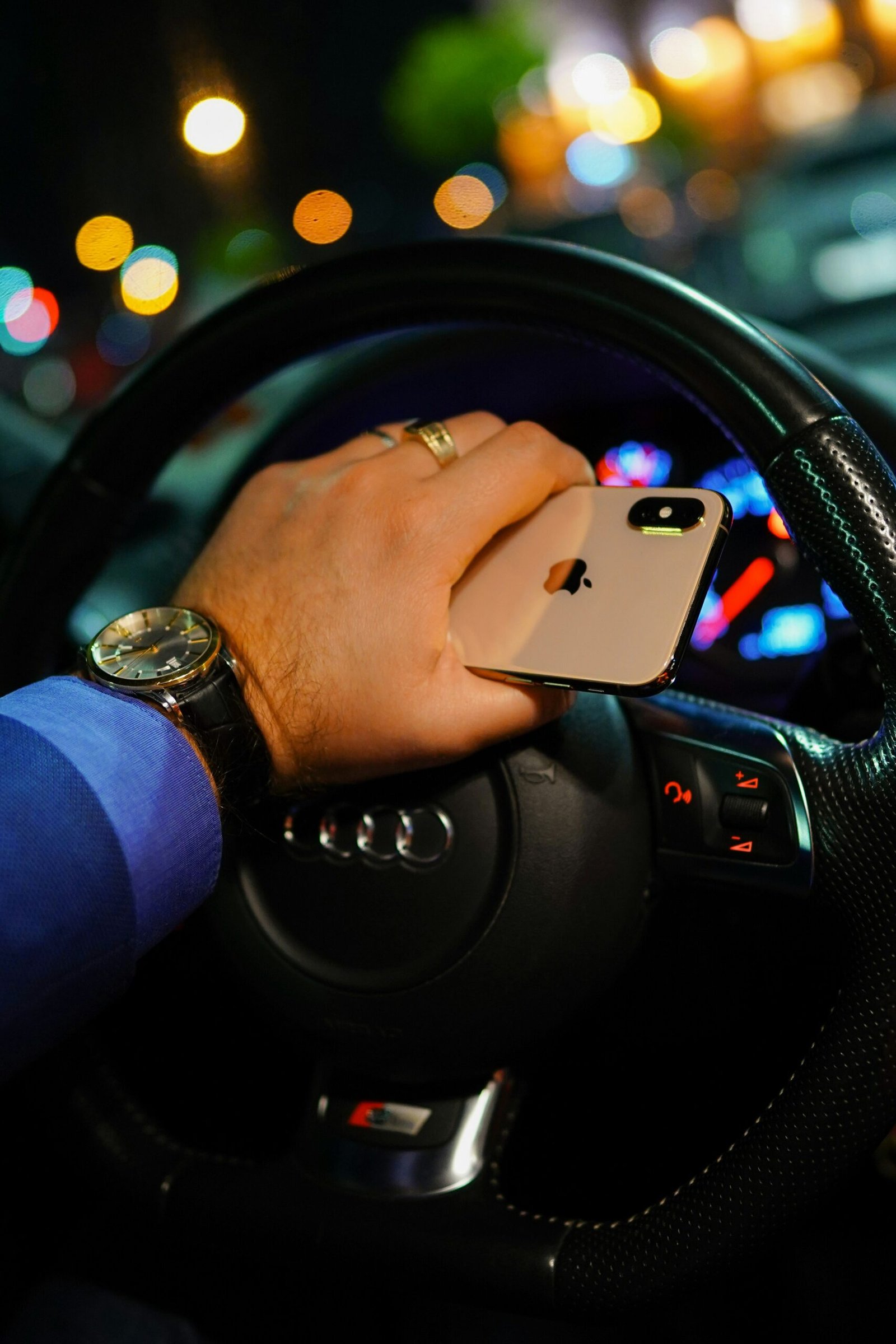 person holding gold iPhone Xs while driving black Audi vehicle