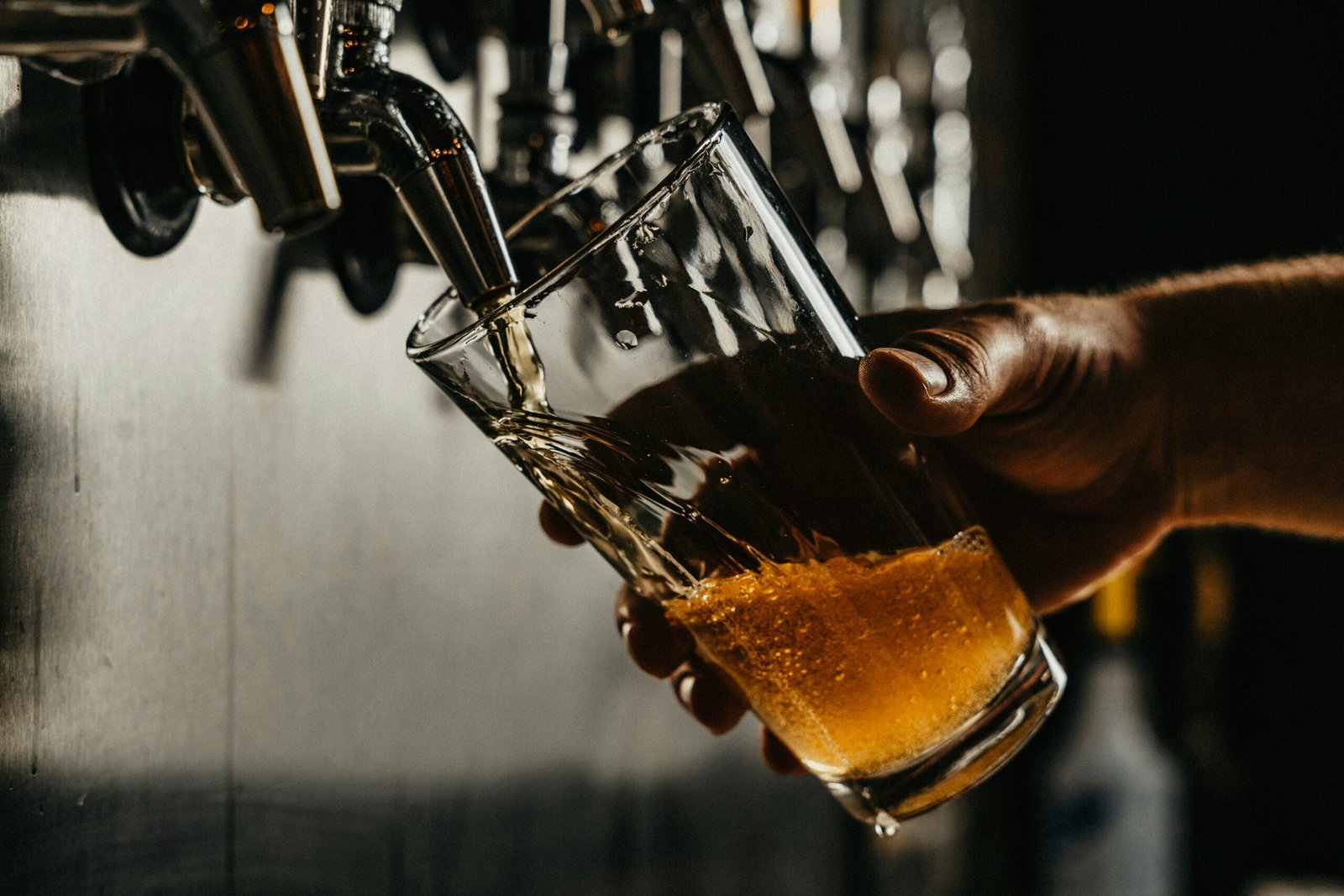 person pouring brown liquid on clear drinking glass